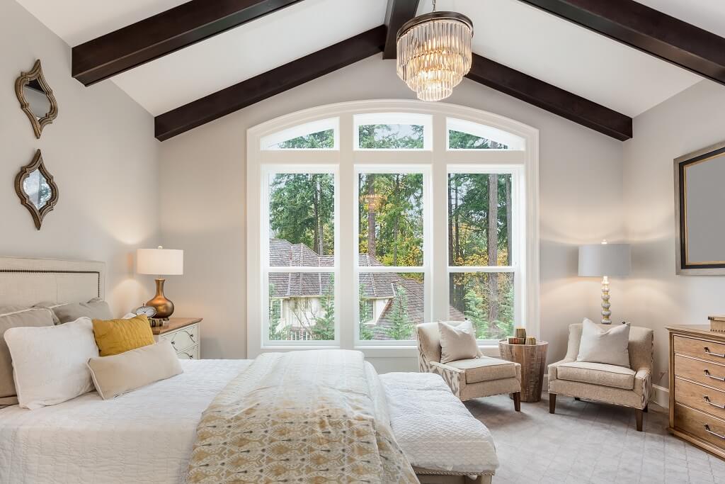 Beautiful furnished master bedroom interior in luxury home . Features vaulted ceiling with wood beams and chandelier.