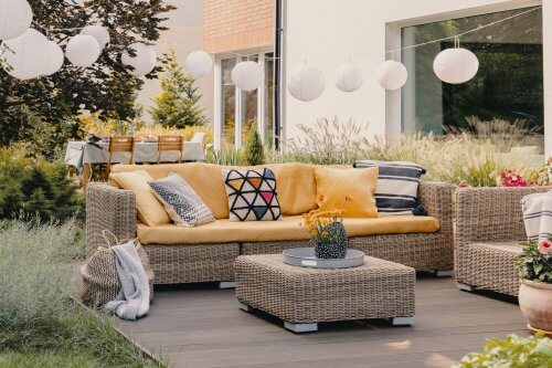 Flowers on rattan table near couch with patterned cushions on the terrace with lanterns. Real photo