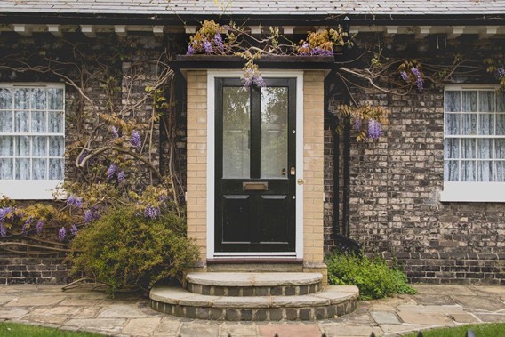 A black front door with a bush on each side and vines with purple flowers climbing the side of the door.