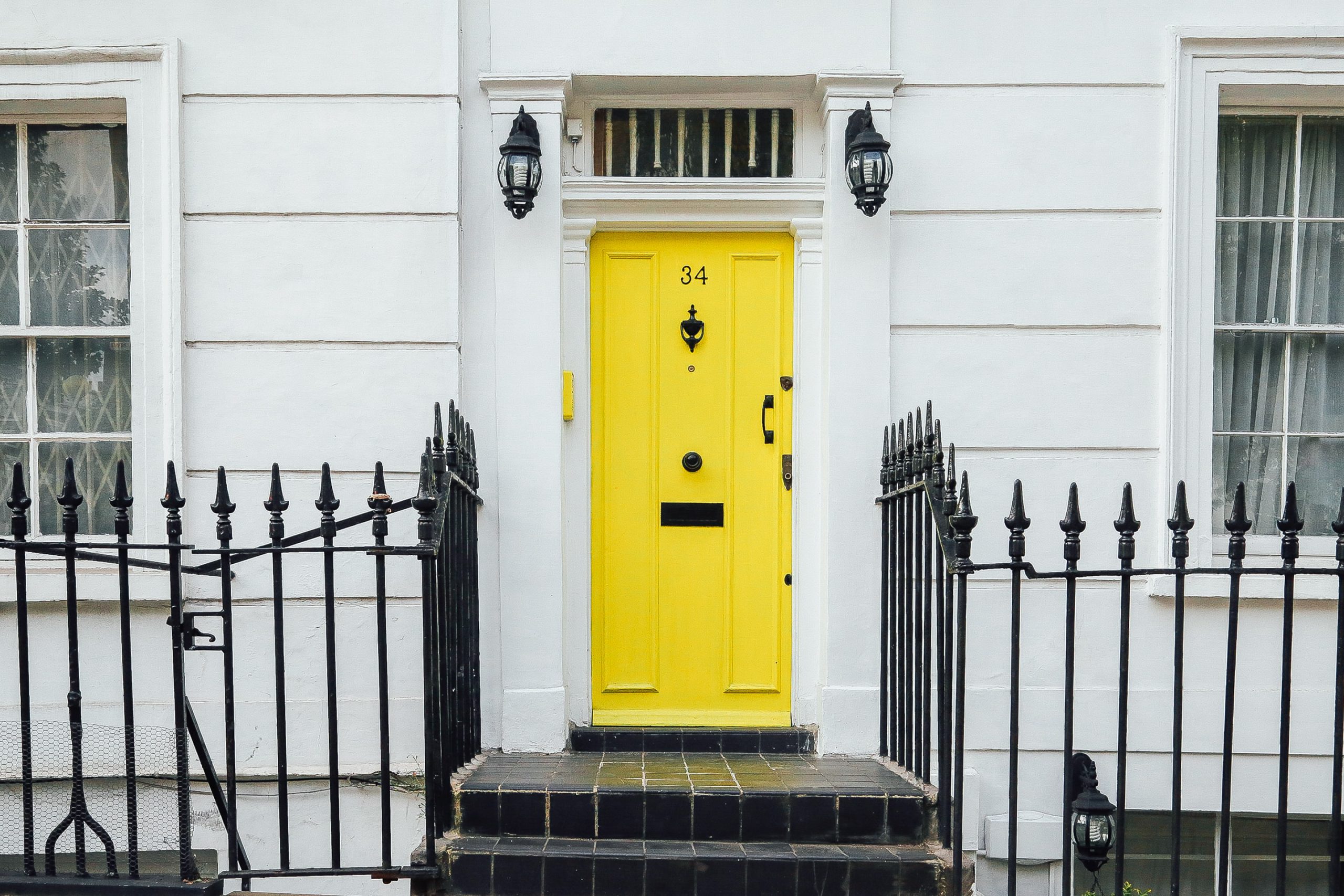 A yellow front door on a white house.