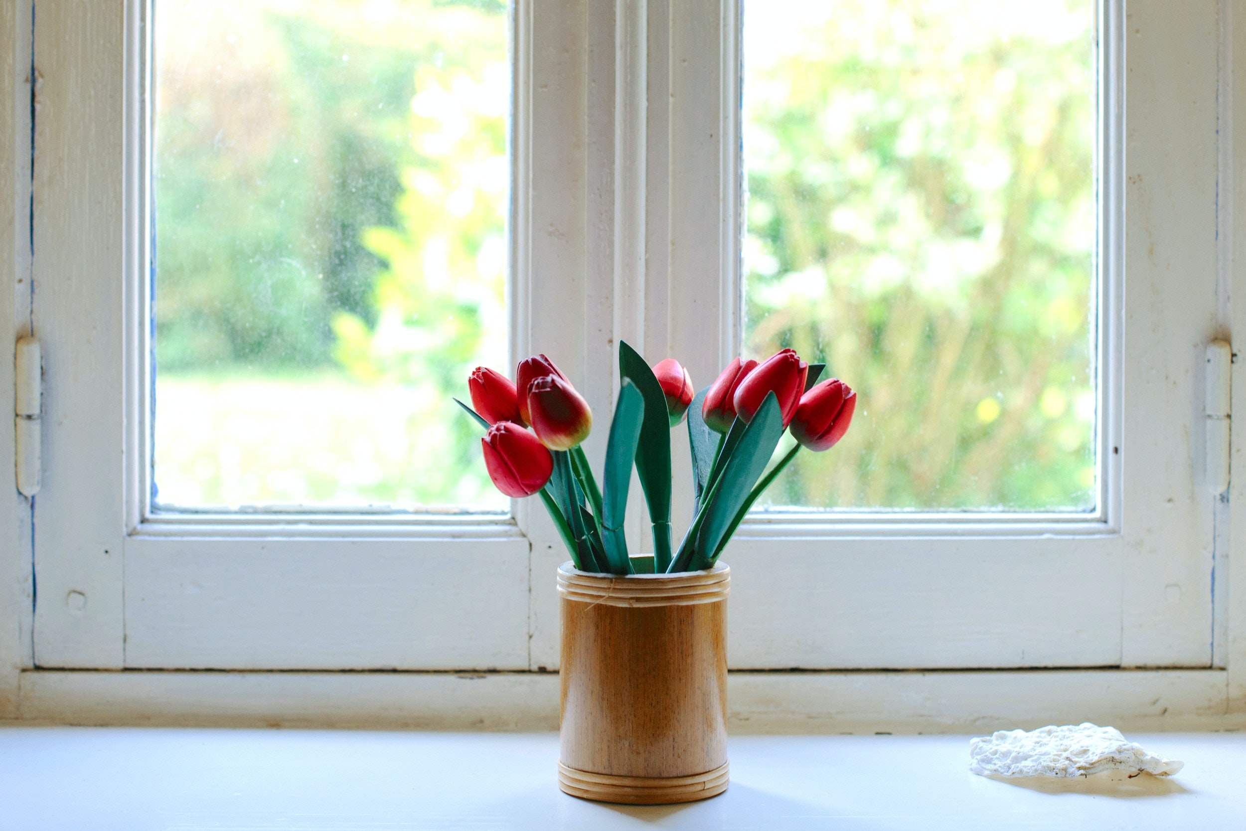 A wooden vase of red tulips in front of a white window.