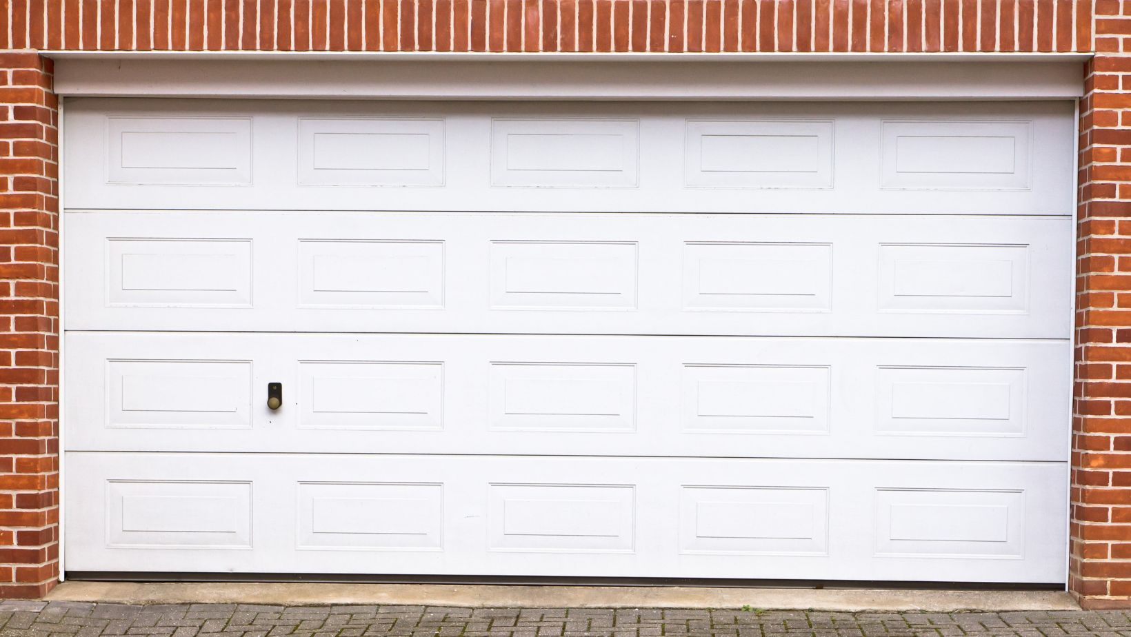 A white garage door surrounded by red brick,