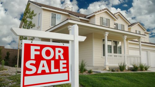 A cream coloured house with a for sale sign out front.