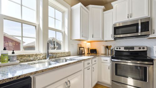 A white kitchen with silver appliances and casement windows.